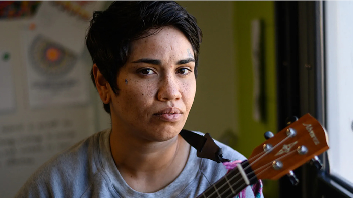 A short haired woman holds a ukulele