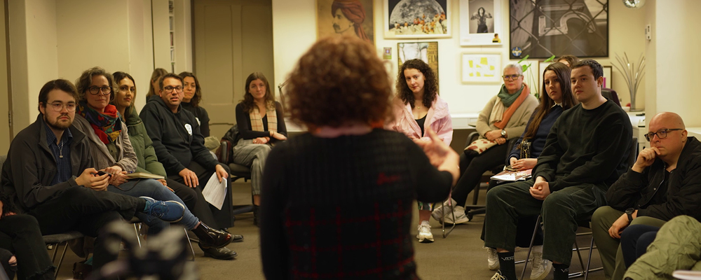 The back of a woman who is speaking to a circle of people.